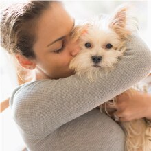 Mulher abraçando cachorro pequeno enquanto usa roupa clara com aspecto limpo e sem pelos.
